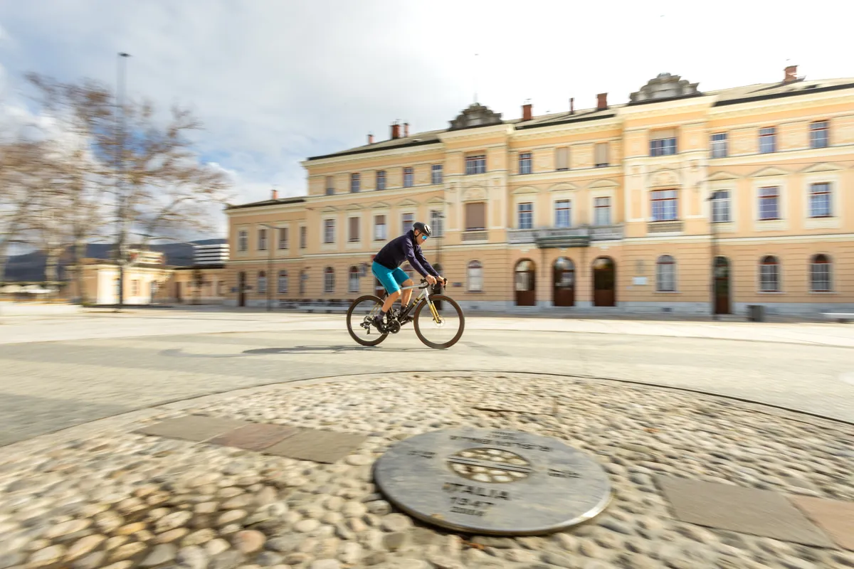 A cyclist crossing Europe Square, the border marker set in the paving, the station behind.